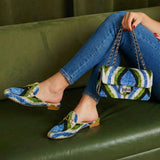 Person wearing blue patterned shoes and holding a matching handbag on a green couch.