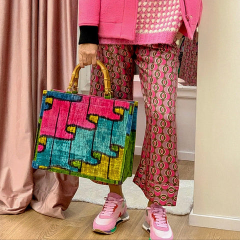Person wearing a pink outfit with a colorful bag indoors.