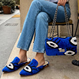 Person wearing blue slippers with eye designs and a matching bag, sitting outdoors.